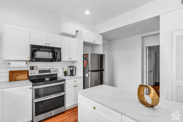 White shaker cabinetry, stainless steel appliances, subway tile backsplash, white countertops, and wood-finish flooring