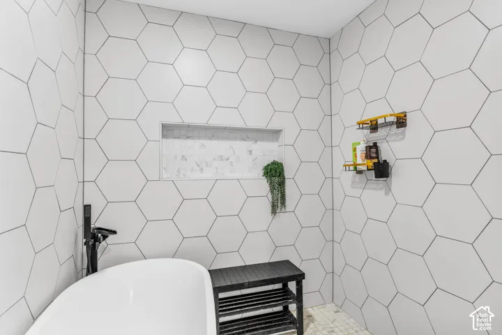 White hexagonal wall tiling, built-in tiled shower niche, and a freestanding soaking tub with a matte black floor-mounted faucet