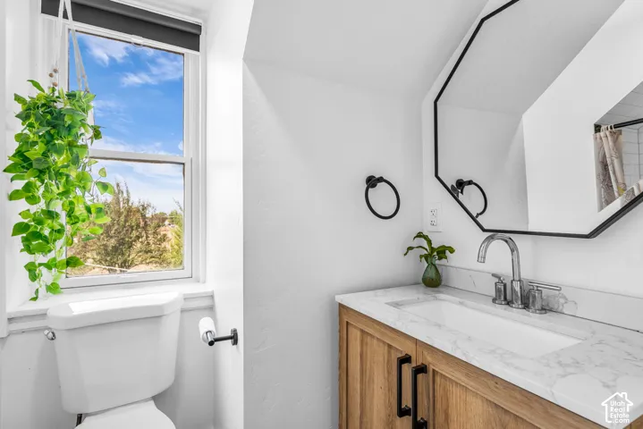 Bathroom featuring a wood-finish vanity with a white rectangular sink, a light-toned countertop, and a black-framed octagonal mirror