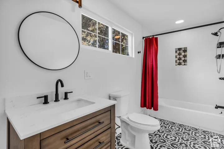 Bathroom featuring patterned floor tiling, single vanity with quartz countertop, black-framed round mirror, and a tiled shower-tub combination with an inset niche