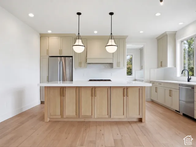 Kitchen featuring a central island with wood cabinetry, light-toned wood-finish flooring, white countertops, stainless steel appliances, and pendant lighting