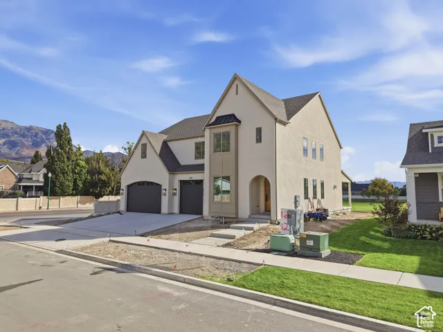 Two-story stucco exterior featuring a prominent arched entryway, multiple gables, and a two-car garage with dark paneled doors