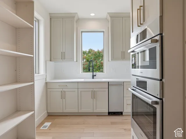 Light wood-finish flooring with built-in shelving, white cabinetry, integrated stainless steel appliances, and a single basin sink
