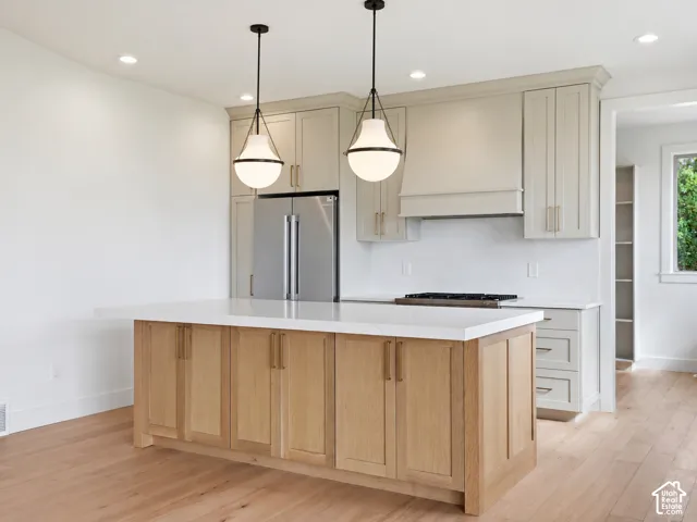 Light wood-finish flooring, a kitchen island with light wood cabinetry, recessed lighting, and pendant light fixtures