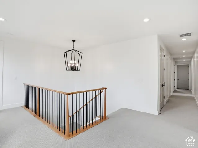 Modern geometric chandelier, recessed lighting, light-toned carpeting, wood handrail, and black balusters