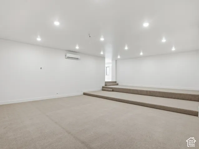 Spacious room featuring neutral carpeting, white walls, recessed lighting, and a wall-mounted climate control unit