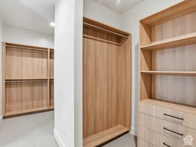 Custom closet system featuring light wood-finish cabinetry, built-in shelving, integrated drawers with black pulls, and chrome hanging rods