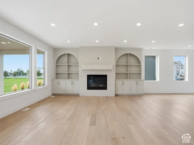 Hardwood flooring, recessed lighting, white brick fireplace, built-in shelving, and large windows
