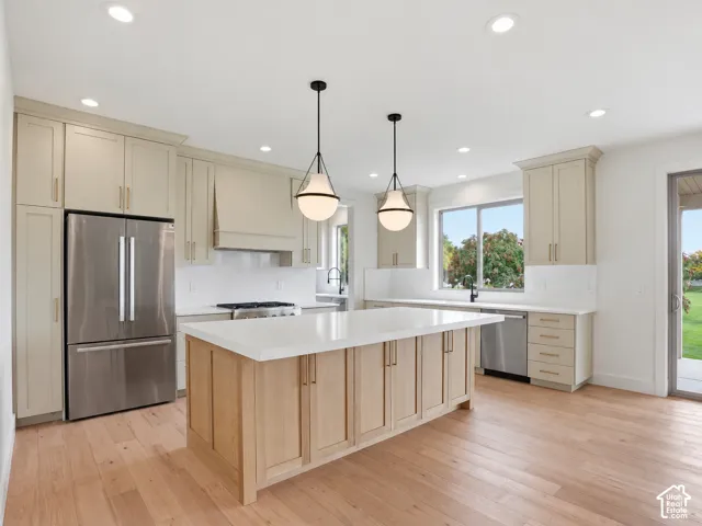 Bright kitchen featuring wood-finish flooring, a central island with a light-toned countertop, stainless steel appliances, and abundant cabinetry