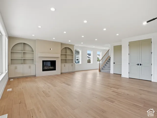 Recessed lighting, wood-finish flooring, built-in shelving, a gas fireplace, and a staircase with wood railing