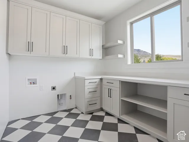 White shaker cabinetry with black hardware, expansive countertop space, checkerboard floor tiling, two floating wall shelves, and a window with a mountain backdrop