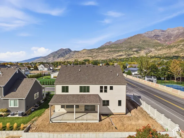 Two-story residence with a covered patio and concrete slab, featuring a shingle roof and a mountain backdrop