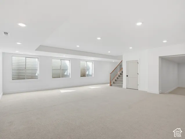 Expansive room with recessed lighting, three windows, light-toned carpet, and a staircase with wood handrails