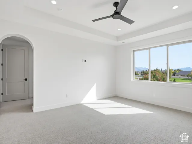 Spacious room featuring carpet flooring, large windows, a tray ceiling, recessed lighting, and a modern ceiling fan