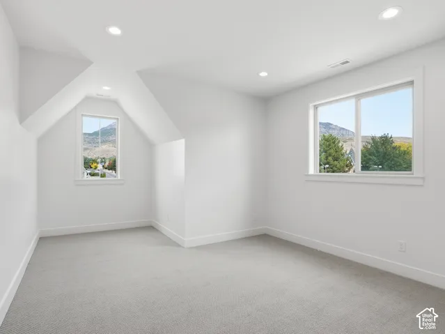 Recessed lighting illuminates a neutral carpeted room with multiple windows
