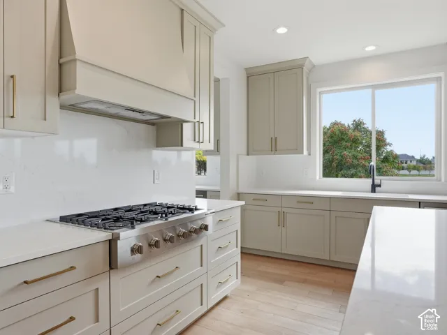 Spacious kitchen featuring light-toned cabinetry, a stainless steel range with a custom range hood, expansive countertops, and wood-finish flooring
