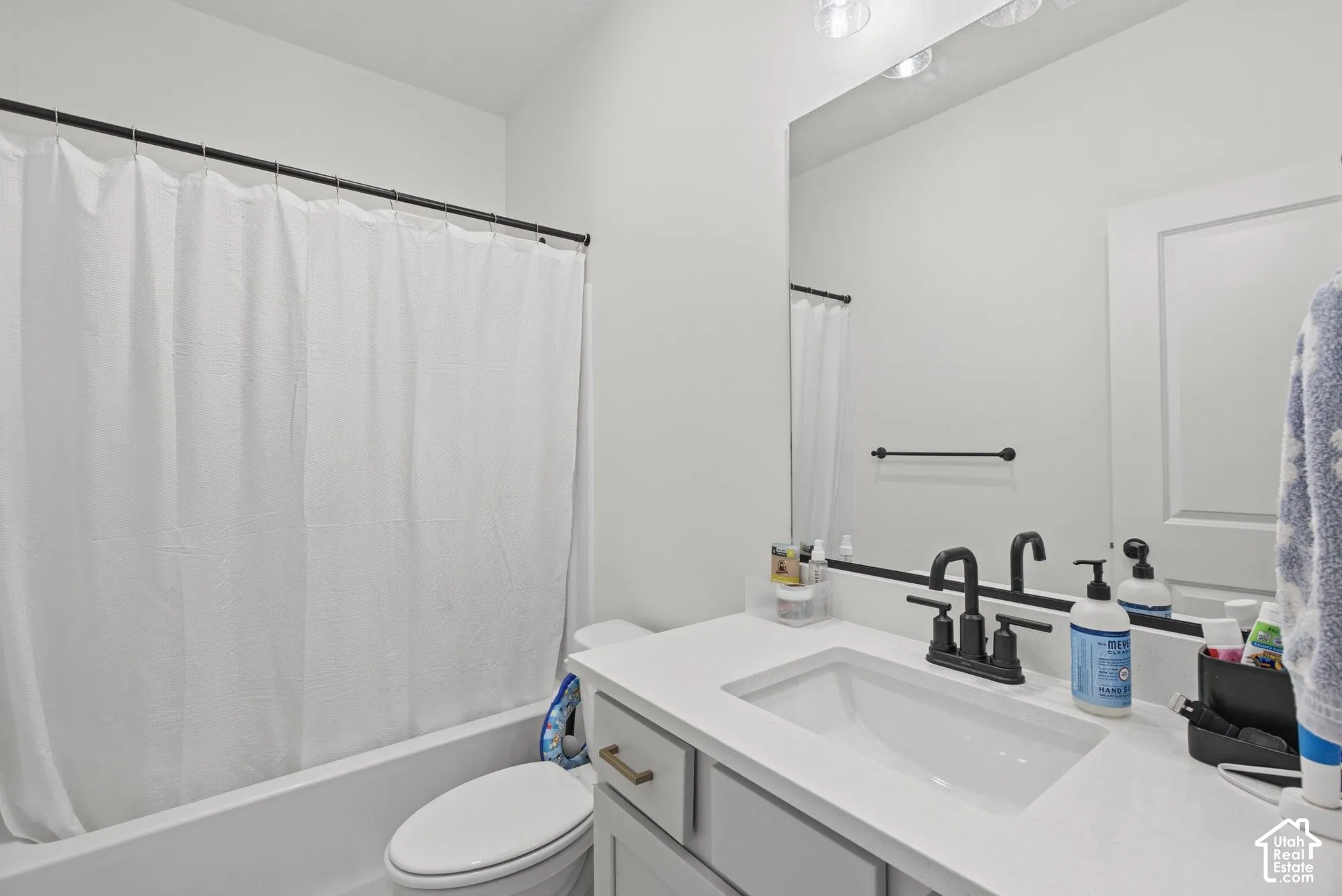 Bathroom featuring a white vanity with an integrated sink, black dual-handle faucet, and overhead lighting