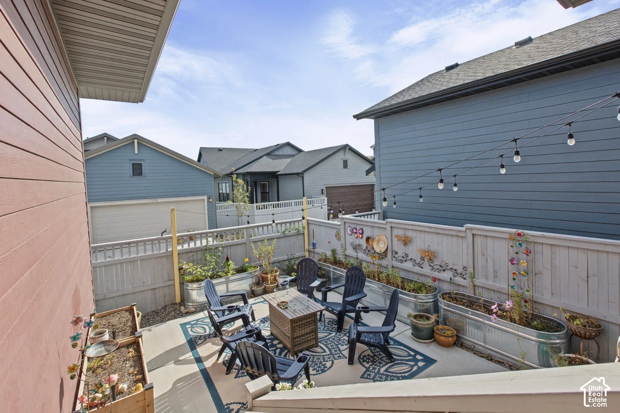 Outdoor patio area with a privacy fence, string lighting, and raised garden beds