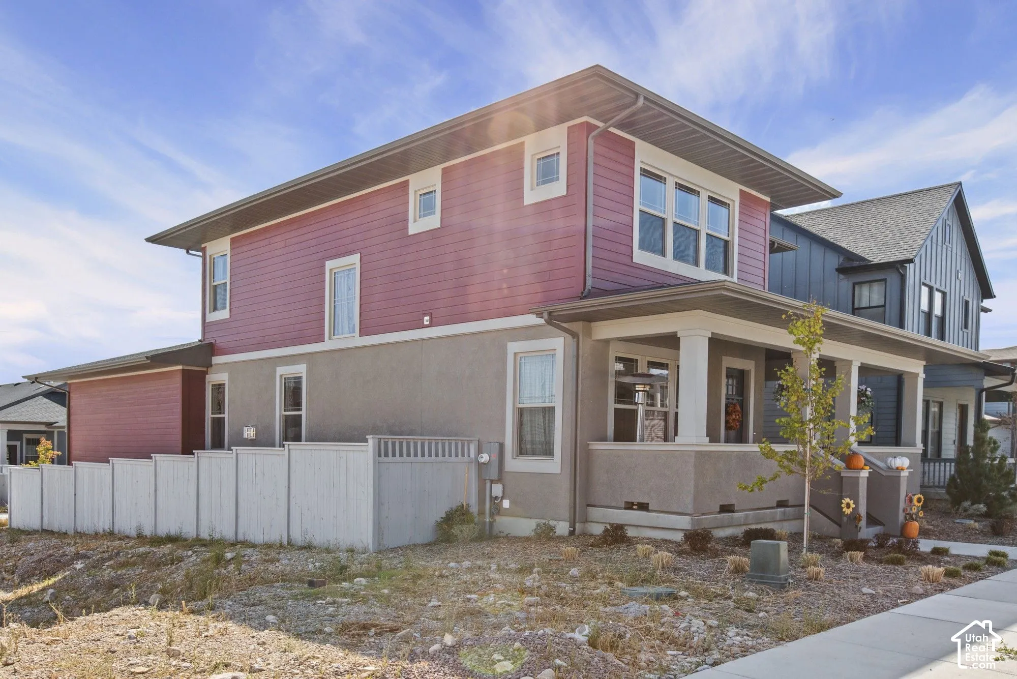 Two-story residence featuring a covered front porch with white columns, red horizontal siding, and grey stucco exterior finishes