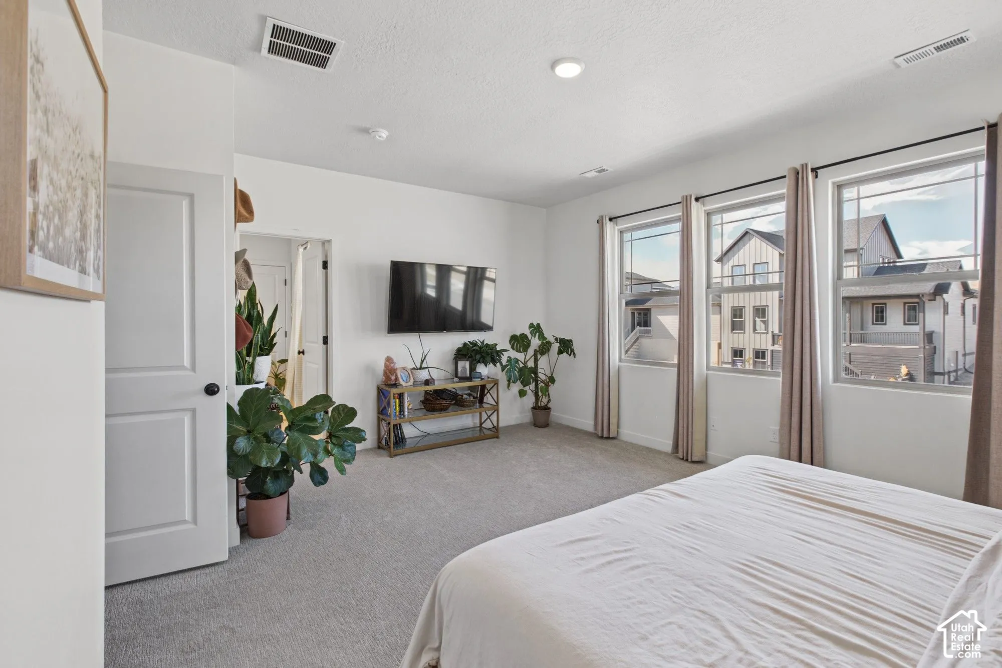 Spacious room featuring light gray carpeting, three large windows with dark rods and light-colored curtains, white walls, and a recessed ceiling light