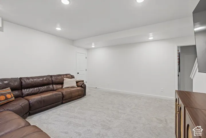 Recessed lighting illuminates a spacious room featuring light-colored carpeting, white walls, and a white interior door with dark hardware
