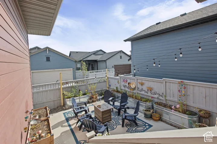 Outdoor patio area with a privacy fence, string lighting, and raised garden beds