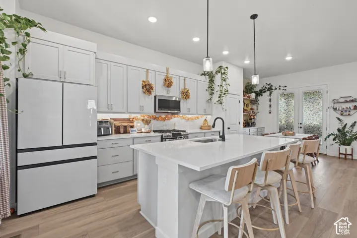 Contemporary kitchen featuring light wood-finish flooring, white cabinetry, integrated stainless steel appliances, a center island with seating, and pendant lighting