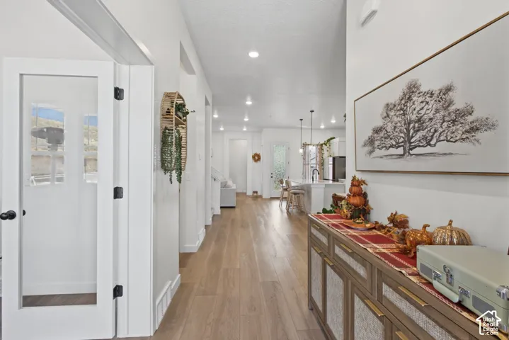 Wood-finish flooring extending through the hallway, white walls, recessed lighting, and a console cabinet with a wood and woven finish
