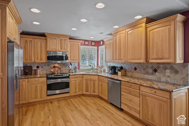 Hardwood flooring, wood cabinetry with crown molding, stone countertops, tiled backsplash, and stainless steel appliances