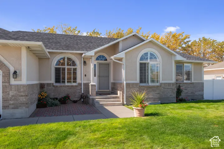 Stucco exterior with a brick-finish facade, architectural shingles, arched windows with plantation shutters, and a well-maintained lawn