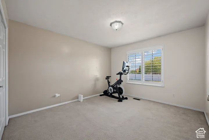 Carpeted room with a ceiling-mounted light fixture and a window featuring white plantation shutters