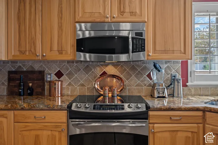 Wood cabinetry, stainless steel microwave, stone tile backsplash with accent tiles, built-in cooktop, and polished countertops