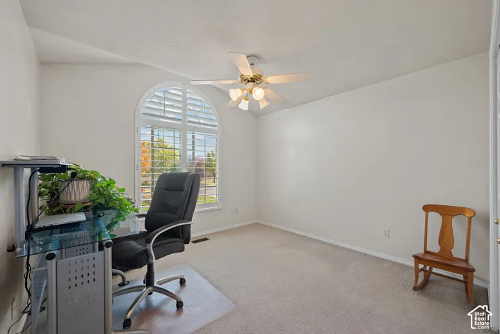 Vaulted ceiling with a ceiling fan, arched window with plantation shutters, and light-colored carpeting