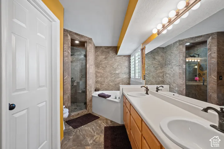 Dual vanity with bronze-finish fixtures, a built-in soaking tub, a tiled walk-in shower with glass enclosure, and tiled flooring