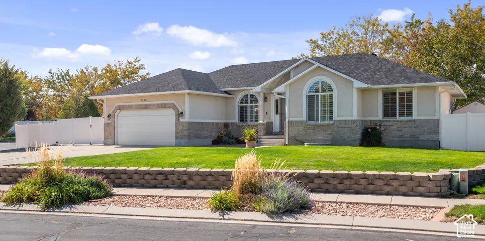 Stucco exterior with stone accenting, arched window features, attached garage, and a manicured lawn