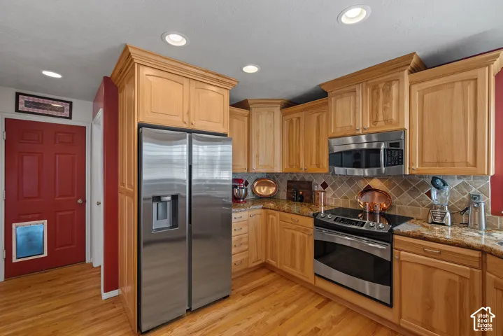 Kitchen featuring wood-finish flooring, recessed lighting, wood cabinetry, stainless steel appliances, and stone countertops with a tiled backsplash
