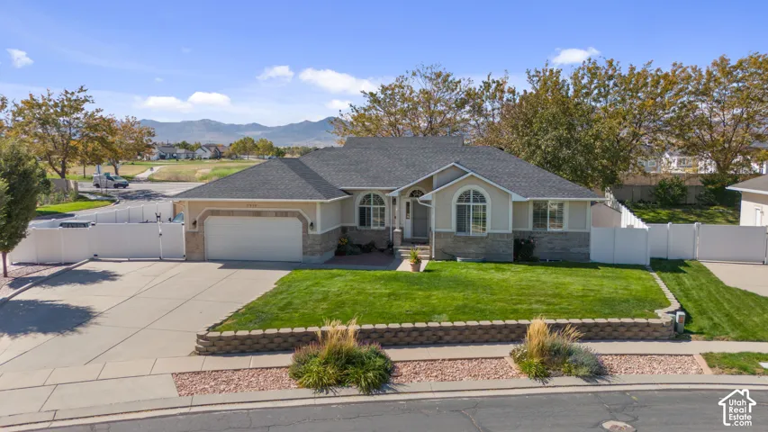 Stucco exterior with stone accenting, arched window, attached garage, manicured lawn, and paved driveway