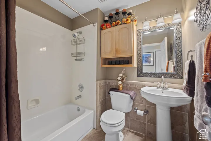 Pedestal sink with chrome faucet, detailed framed mirror, three-light vanity fixture, built-in wooden cabinet, and tiled wainscoting