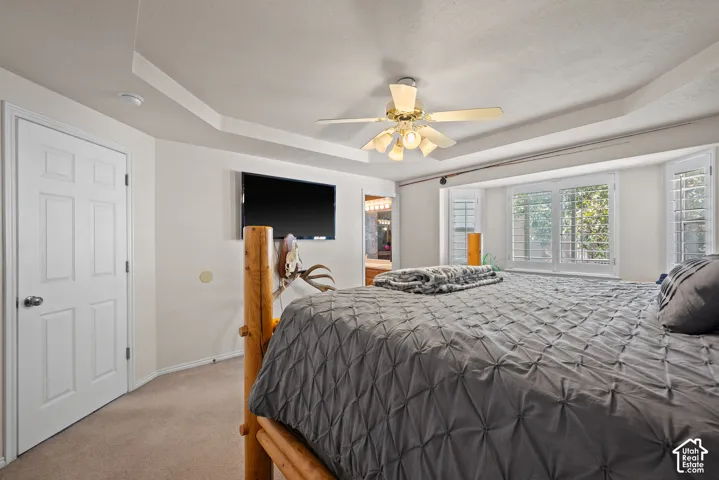 Tray ceiling with recessed lighting, ceiling fan, and bay window with white plantation shutters