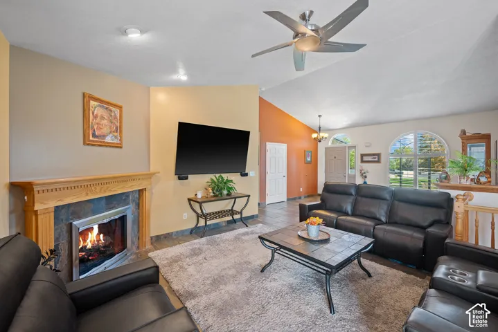 Vaulted ceiling with a ceiling fan, fireplace with a wood mantle and stone surround, tile flooring, and arched windows