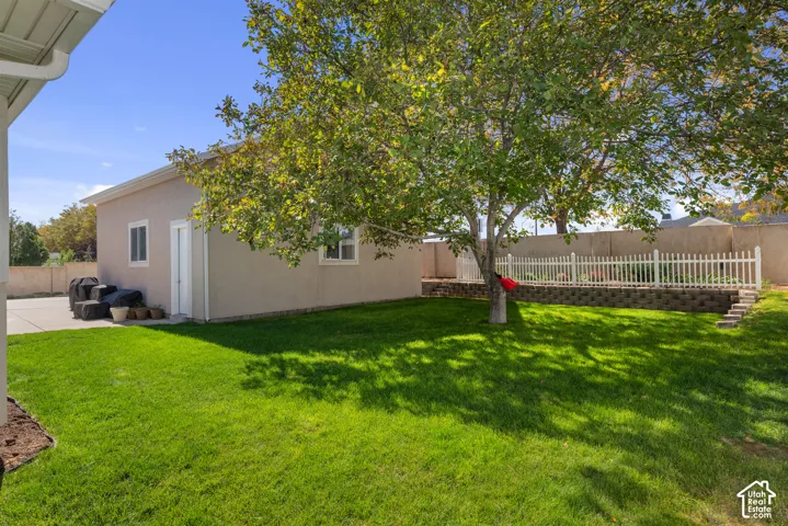 Expansive grassy yard with mature tree, concrete patio, and white picket fence