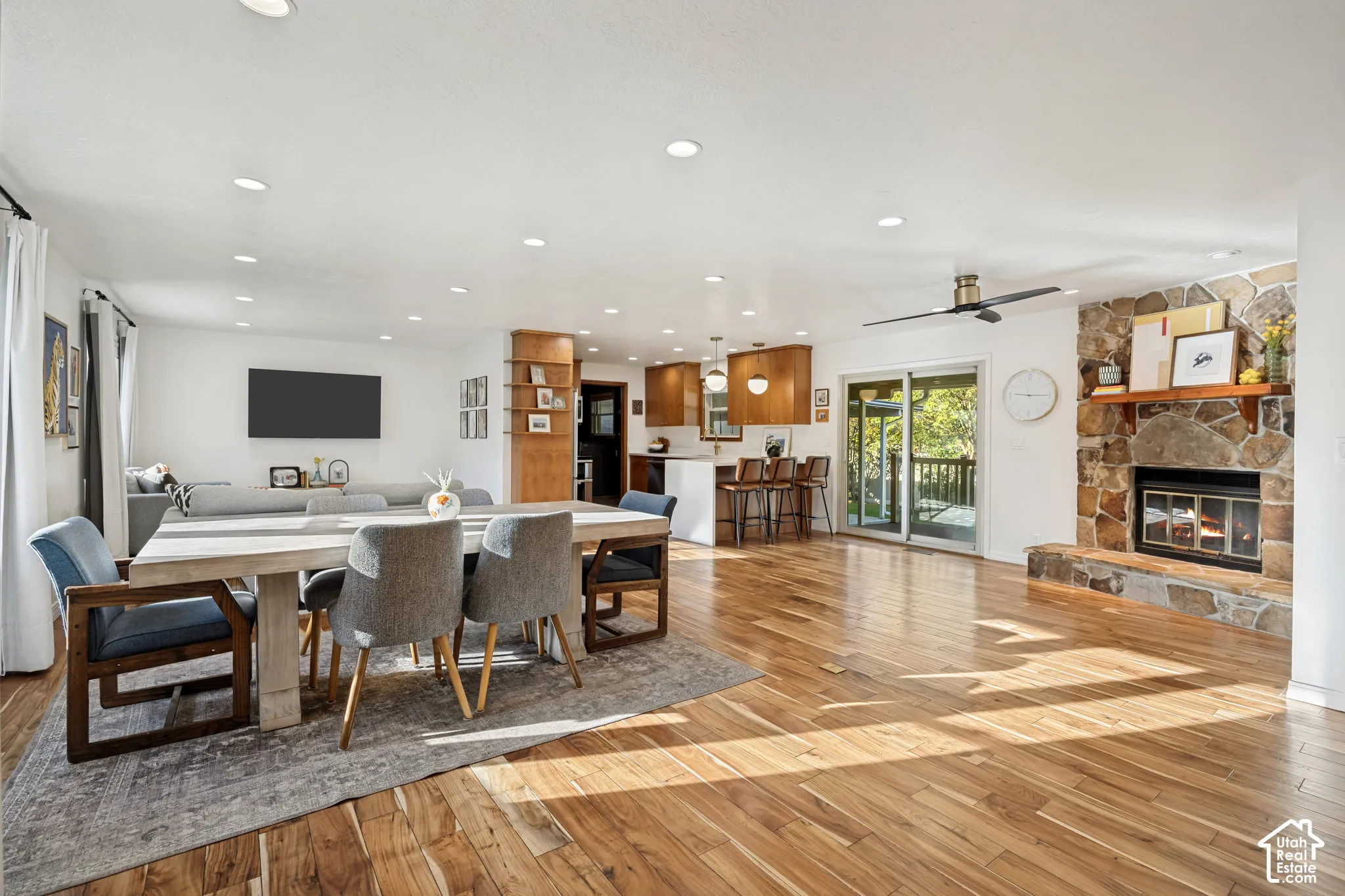Open-concept interior featuring wood-finish flooring, a stone fireplace, recessed lighting, and a sliding glass door