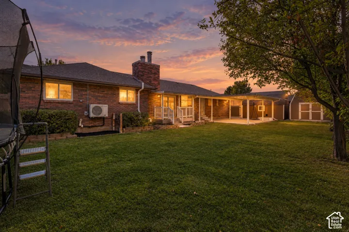 Brick exterior with a covered patio, expansive lawn, and exterior storage shed
