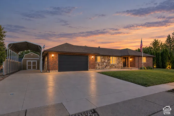 Brick and stone exterior with an attached garage, covered carport, and a detached shed