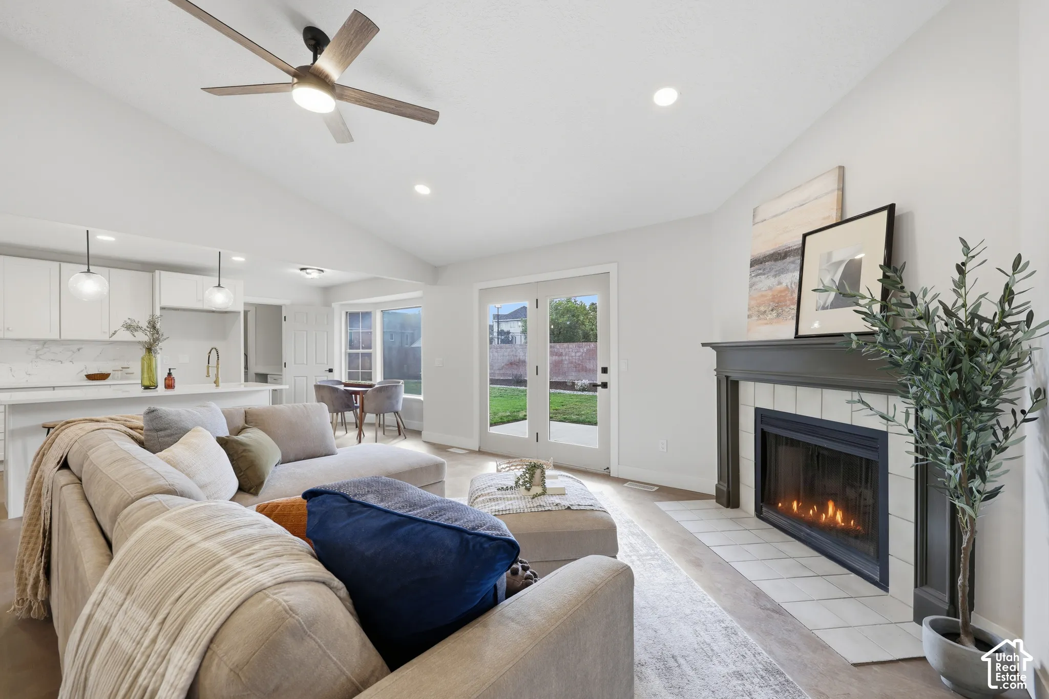 Vaulted ceiling with a ceiling fan, recessed lighting, fireplace with a tiled hearth and wood mantle, French doors to the exterior, and wood-finish flooring