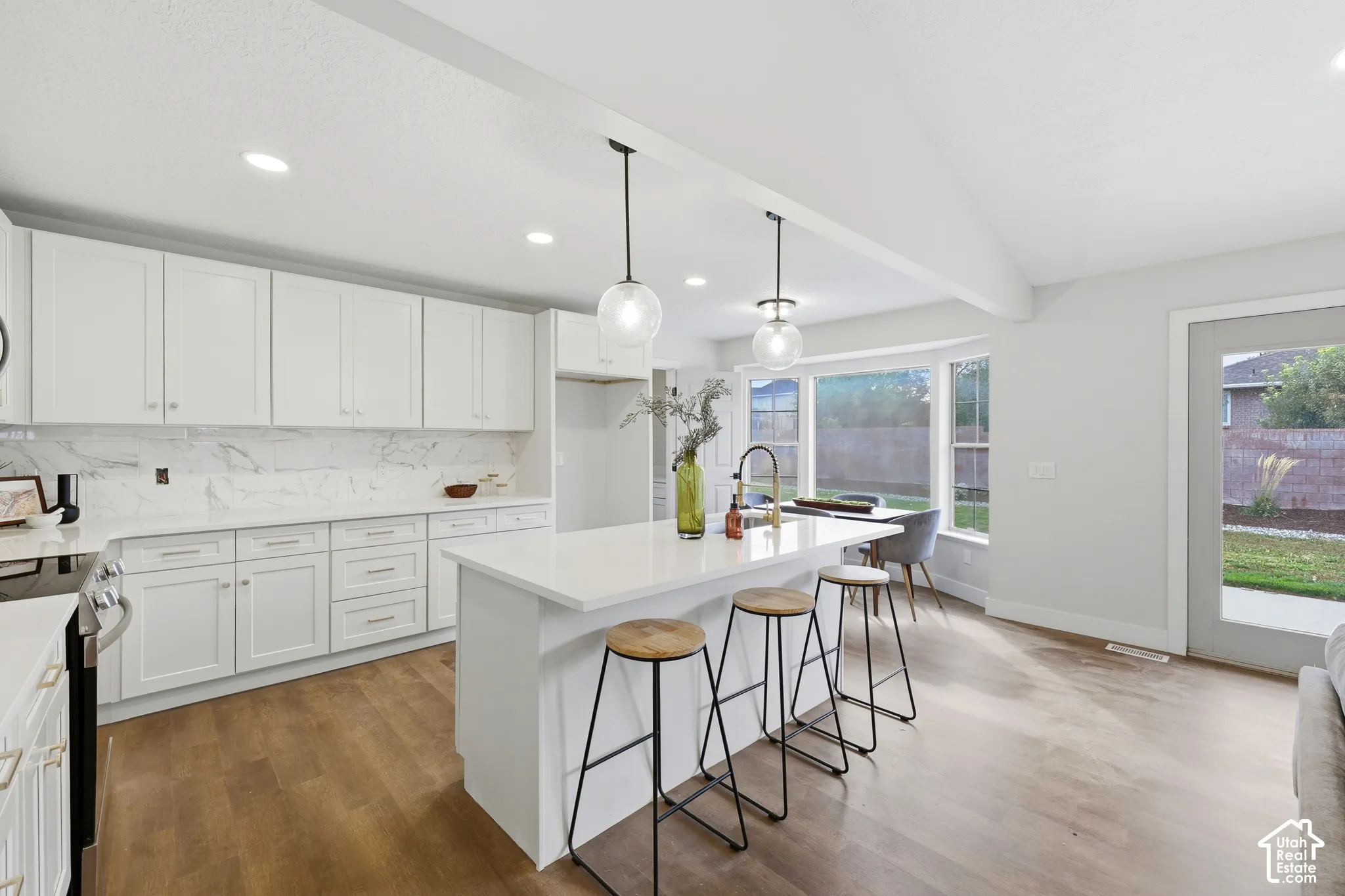 Modern kitchen featuring white cabinetry, a large kitchen island with pendant lighting, a full suite of stainless steel appliances, and wood-finish flooring
