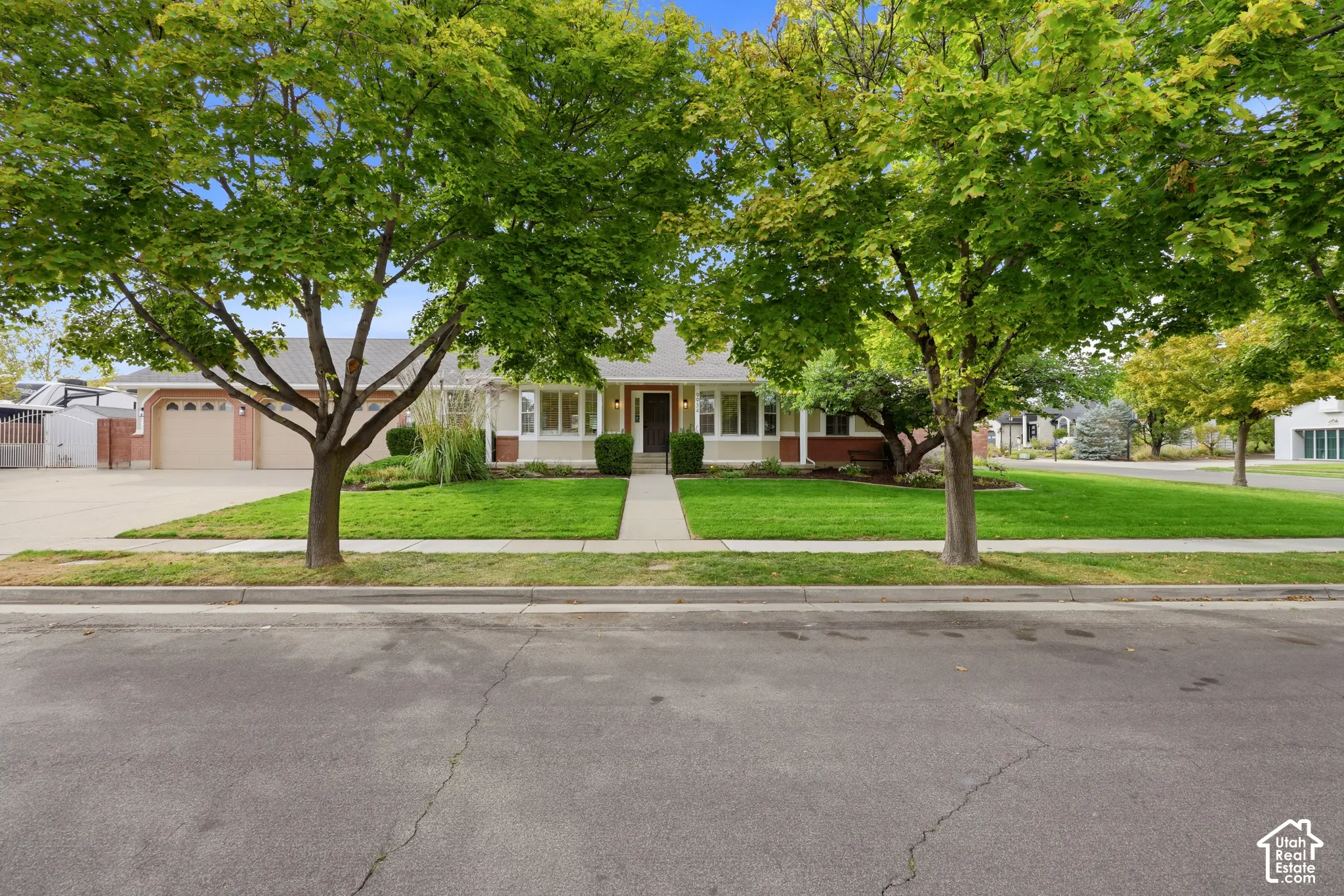 Single-story residence featuring a two-car garage, manicured lawn, and mature trees