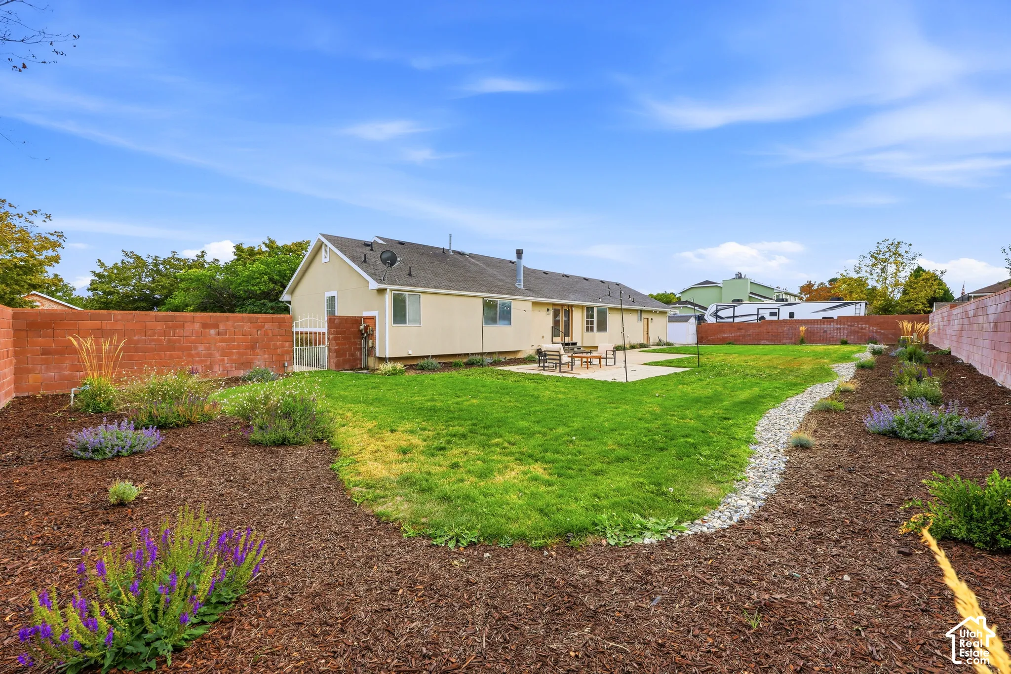 Expansive backyard featuring a manicured lawn, concrete patio, a rock-lined dry creek bed, and landscaped garden beds with mulch and plantings