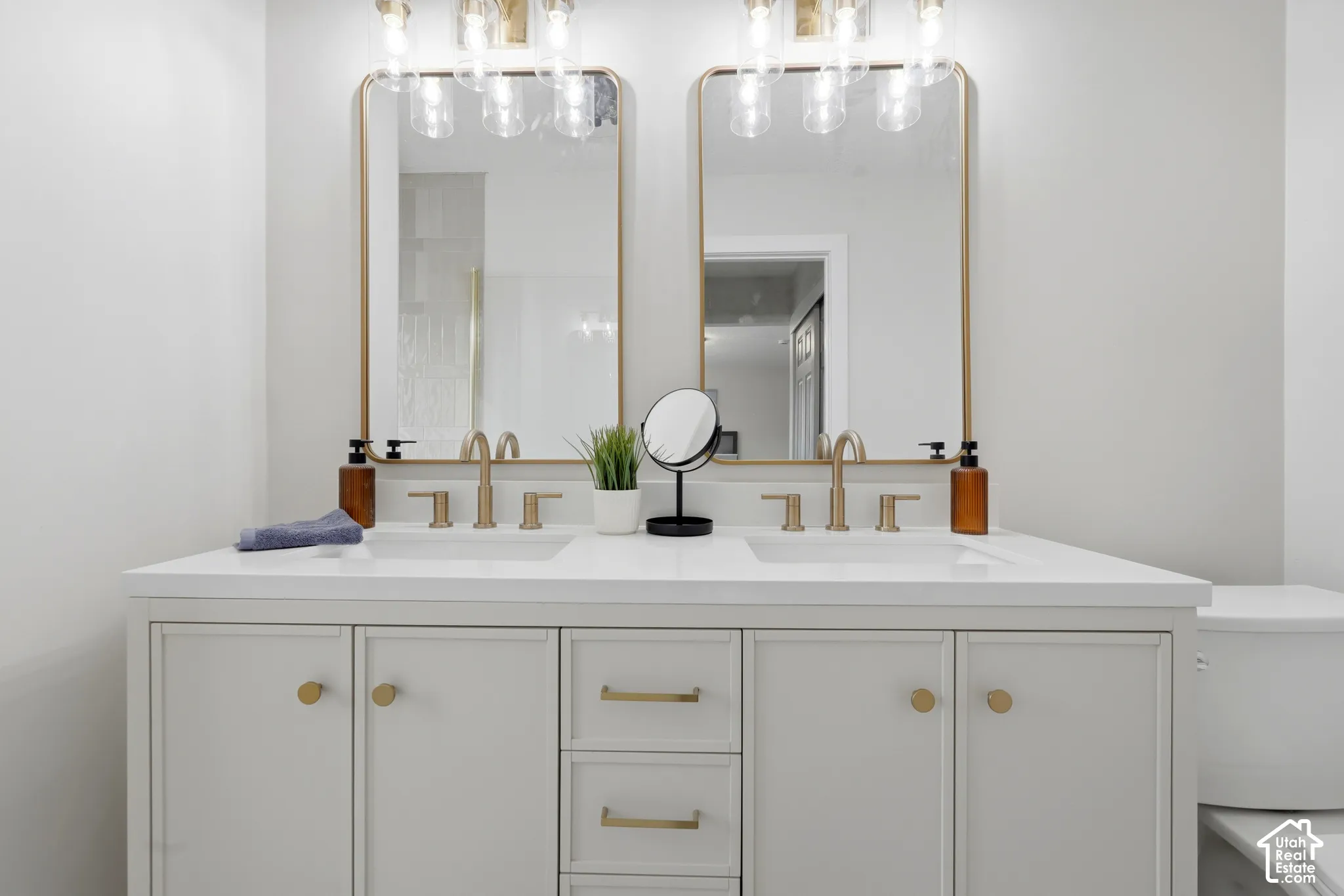 Double vanity with integrated sinks, white countertop, gold-finish hardware, and dual gold-framed mirrors