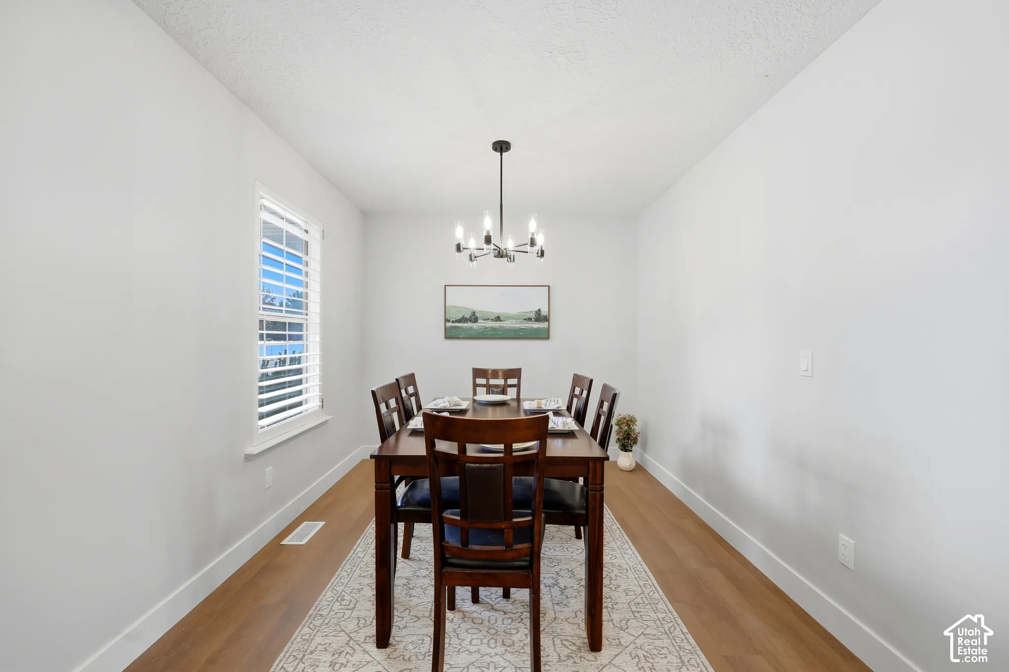 Recessed dining space featuring a window with white blinds, wood-finish flooring, and a contemporary chandelier